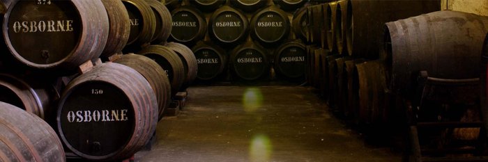 Ein Blick auf eine Reihe von Holzfässern, die ordentlich gestapelt sind, mit dem Namen 'OSBORNE' deutlich sichtbar auf jedem Fass.