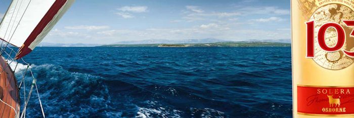 Ein elegantes Segelboot fährt über das glitzernde Wasser, umgeben von einer malerischen Landschaft und einem klaren Himmel und einer 103 Flasche.