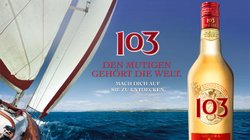 Ein Segelboot gleitet über das blaue Wasser, während eine Flasche des Getränks 103 im Vordergrund steht.