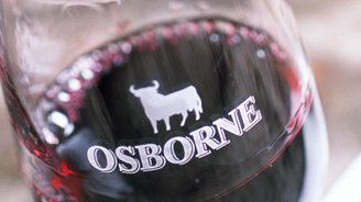 Nahaufnahme eines Weinglases mit 'OSBORNE'-Logo und Rind, umgeben von einem rustikalen Tisch und verschwommenen Papieren.