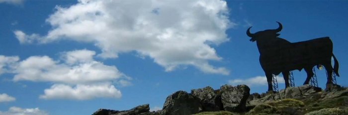 Der Silhouette eines Stiers, die sich gegen einen strahlend blauen Himmel abhebt, während Wolken sanft vorbeiziehen.