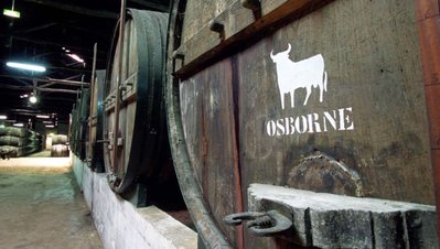 In einem dunklen Lagerraum stehen große Holzfässer, eines mit dem weißen Osborne-Bullen-Logo und dem Schriftzug 'OSBORNE'.