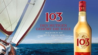 Ein Segelboot gleitet über das blaue Wasser, während eine Flasche des Getränks 103 im Vordergrund steht.