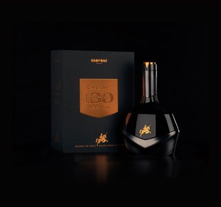 Ein hochwertiger Brandy in einer einzigartigen Flasche, die zusammen mit einer festlichen Verpackung in einem dunklen Ambiente präsentiert wird.